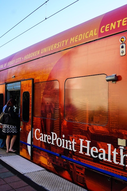 Commuters boarding NJ Transit train with CarePoint Health advertisement